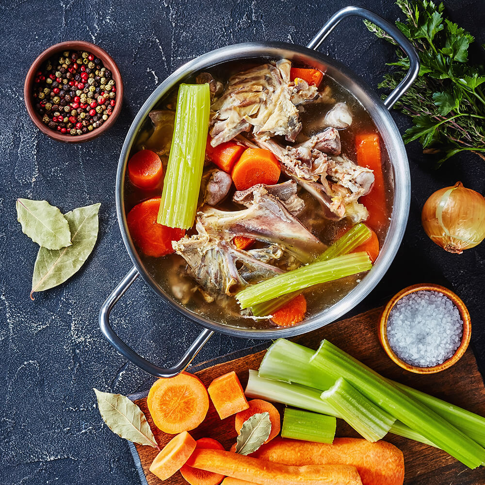 cooking chicken stock with vegetables and aromatic herbs in a metal stockpot, ingredients on a kitchen worktop, flat lay, free space left